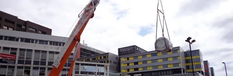 A scanner being lifted by crane into a hospital building
